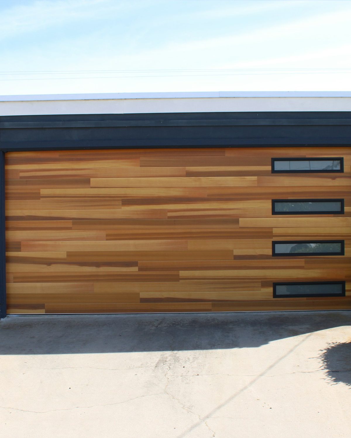 Garage door finished in warm horizontal wood grain against a dark charcoal facade