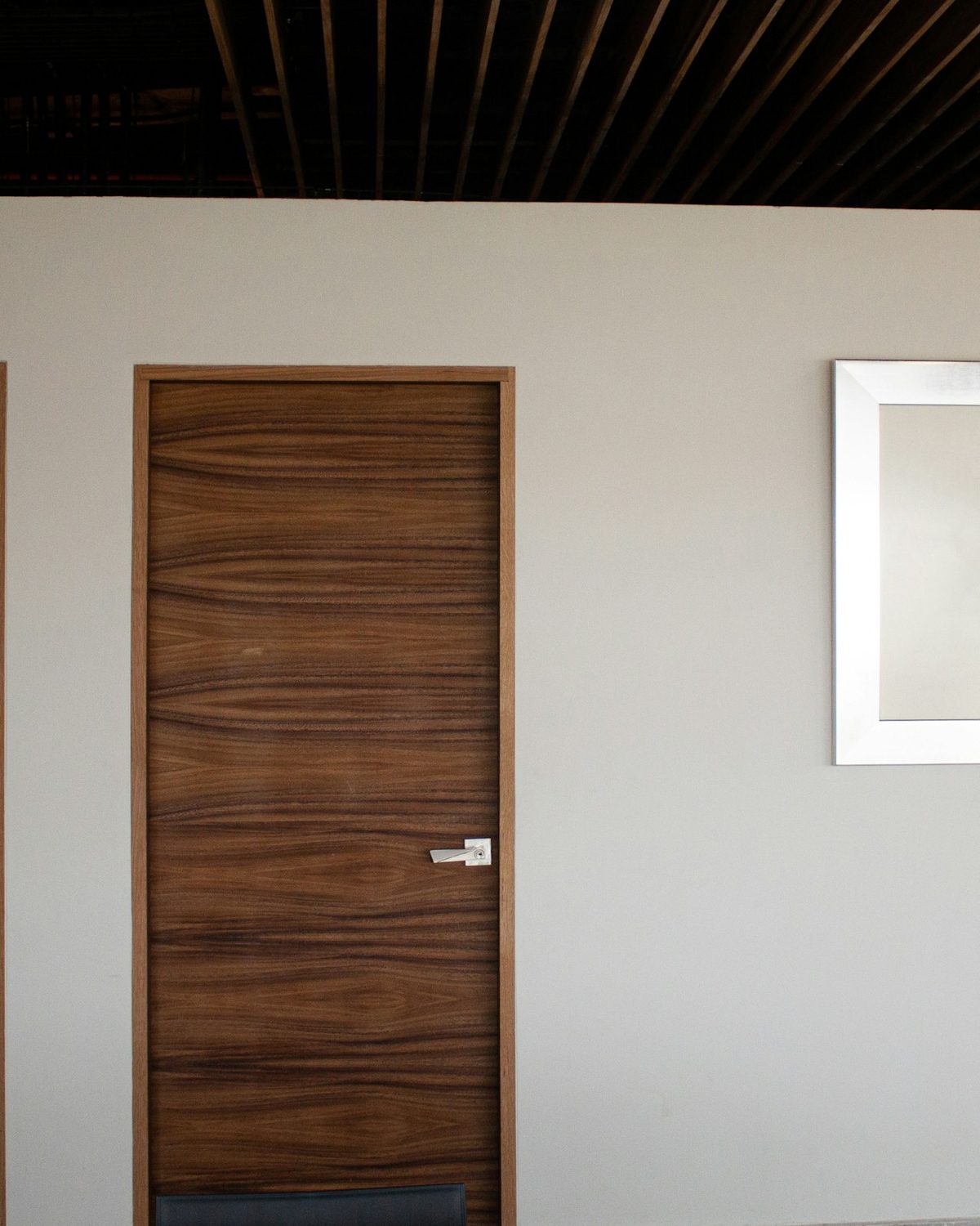 Interior door in figured walnut grain below a slatted wood ceiling